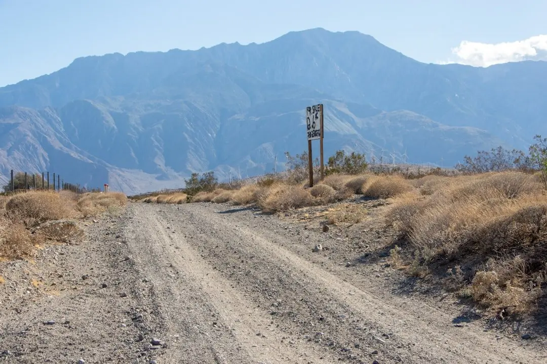 Dirt road stretching toward mountain range beneath clear blue sky Dirt road stretching toward mountain range beneath clear blue sky